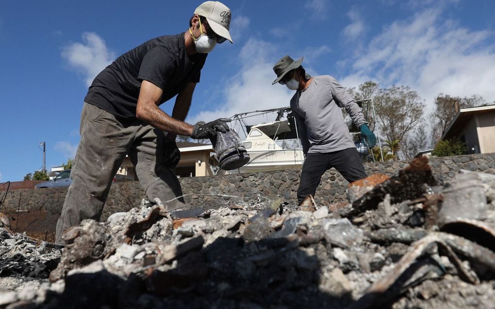 Bewoners Brook Cretton (l.) en Spencer Kim (r.) doorzoeken het puin van een huis dat door een bosbrand werd verwoest in Kula, op het eiland Maui. beeld AFP, Justin Sullivan