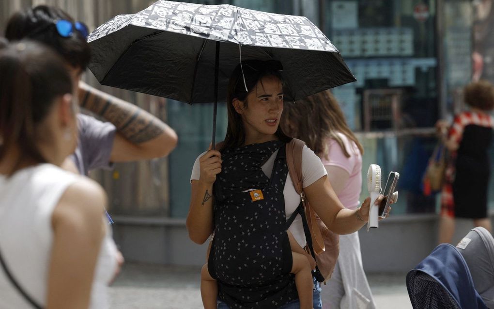 Een vrouw beschermt zichzelf tegen de hitte met een paraplu en een draagbare ventilator. beeld AFP, Javier Soriano