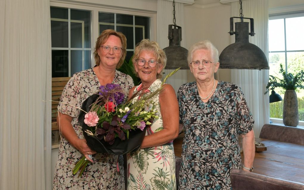 Ina van der Vegte (l.) geeft haar zus Marrie Bakker, die in het midden staat, een bos bloemen omdat ze altijd paraat staat om haar moeder, Jent Wastenecker (r.) te helpen.