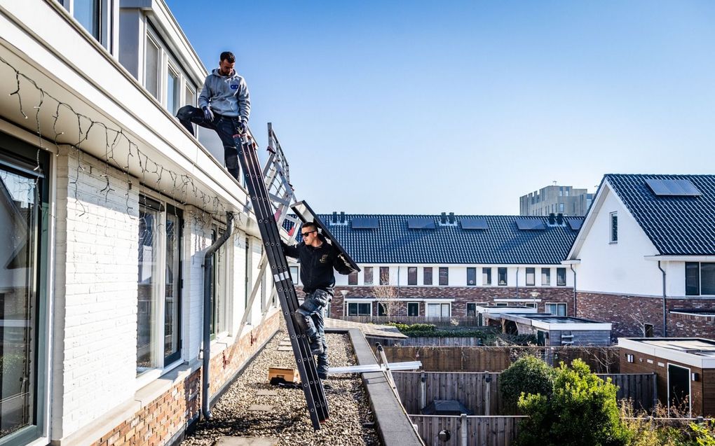 Installateurs plaatsen zonnepanelen op een dak van een woning in Vlaardingen. Op zonnige dagen zorgt de massaal  teruggeleverde zonne-energie regelmatig voor problemen op het elektriciteitsnet. beeld ANP, Jeffrey Groeneweg