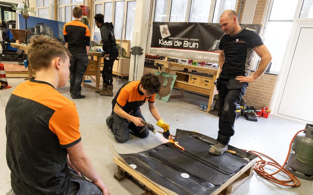 Een medewerker van Klaas de Bruin dak- en gevelbekleding brengt de jongens de basisbeginselen van het dakbranden bij. beeld RD, Anton Dommerholt