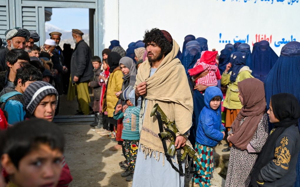 Volledig bedekte Afghaanse vrouwen wachten onder toeziend oog van de taliban met hun kinderen op een voedselpakket van Unicef. beeld AFP, Wakil Kohsar