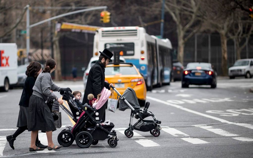 Een joodse man en twee vrouwen duwen kinderwagens voor zich uit terwijl ze een straat oversteken in de Joodse wijk van Brooklyn in New York City. De burgemeester van New York heeft een vaccinatieplicht afgekondigd. beeld AFP, Johannes Eisele