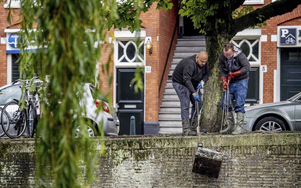 Magneetvisser Glenn van den Brekel (l.) en een helper halen een apparaat boven water in Den Haag. beeld ANP,  Robin Utrecht