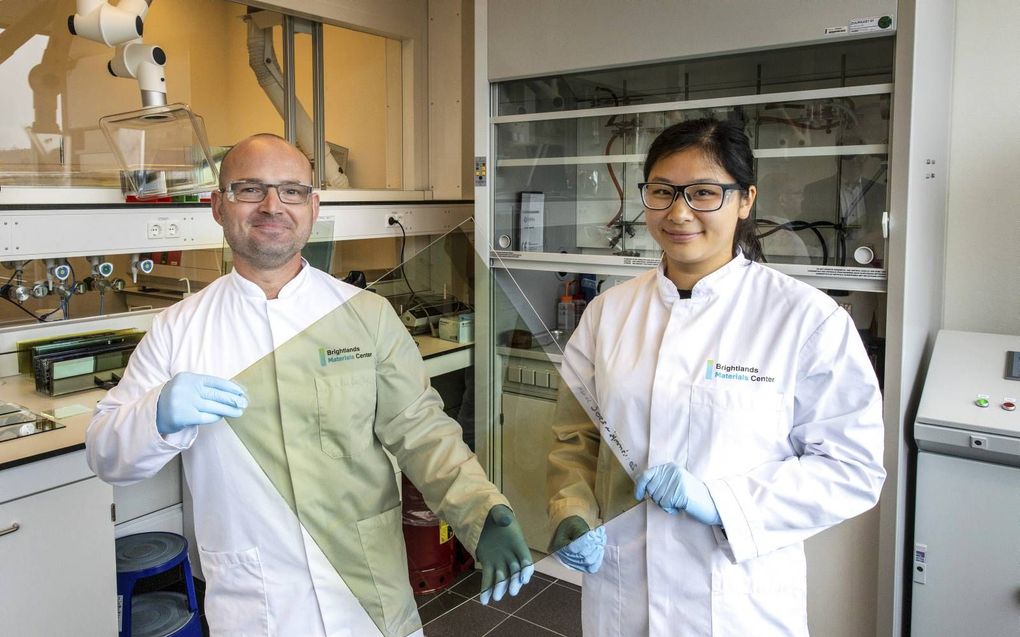 Het gecoate, thermochrome glas komt lichtbruin uit het dompelbad. Laboranten Roberto en Cindy tonen een ruit van 50 bij 50 centimeter, waarmee ze laboratoriumproeven uitvoeren. beeld RD, Henk Visscher