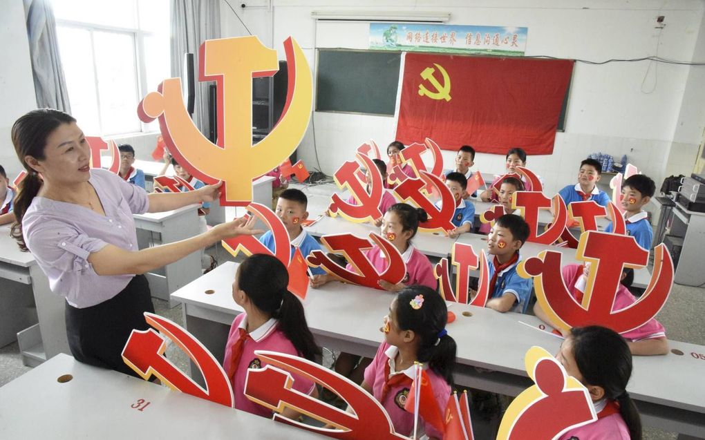 De Chinese overheid doet er alles aan om westerse invloeden door buitenlandse leerkrachten tegen te gaan. Foto: een klas poseert met het embleem van de Communistische Partij. beeld STR/AFP