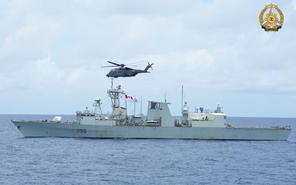 Militair vaartuig in oceaan, helikopter vliegt ervoor.