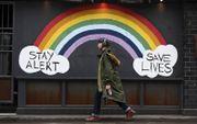 Een man loopt in de Britse hoofdstad Londen langs een regenboog met tekst om alert te blijven op het voorkomen van coronabesmettingen. beeld EPA, Andy Rain