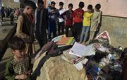 Kinderen in Kabul kijken naar restanten van schoolboeken, schriften en schoenen nadat zaterdagmiddag hun school door drie aanslagen was getroffen. Daarbij vielen zeker 58 doden.  beeld AFP, Wakil Kohsar.