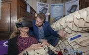 Een medewerker van Philip Nitschke demonstreert een eerdere versie van de Sarco op een Uitvaartbeurs in Amsterdam, april 2018. Met een virtuele bril konden bezoekers ervaren hoe het is om in de capsule te liggen. beeld Hollandse Hoogste, Sabine Joosten