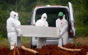 Gekleed in beschermende pakken begraven Indonesische uitvaartmedewerkers een overleden coronapatiënt. beeld EPA, Adi Weda