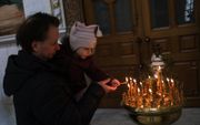 Een Oekraïense man en zijn zoontje branden een kaarsje in de orthodoxe kathedraal in Odessa, die valt onder het patriarchaat van Moskou. beeld EPA, Sedat Suna