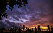 Mensen kijken naar de zonsondergang langs de Marine Drive-promenade terwijl moessonwolken boven de kust van de Arabische Zee in Mumbai zweven. beeld EPA, Divyakant Solanki