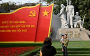 Een man en een kind laten zich fotograferen voor een monument in de Vietnamese hoofdstad Hanoi. De Communistische Partij van Vietnam (CPV) heeft de touwtjes stevig in handen in het land. beeld AFP, Manan Vatsyayana