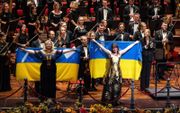 Sopraan Liudmyla Monastyrska (l.) en pianiste Anna Fedorova tijdens het applaus met de Oekraïense vlag. Rechts dirigent Keri-Lynn Wilson. beeld ANP, Ramon van Flymen 