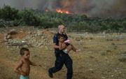 Griekse politieagent evacueert een kind uit een dorp in de buurt van Athene. beeld AFP, Aris Messinis