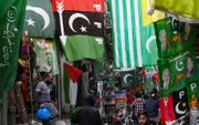 Mensen lopen langs vlaggen van Pakistaanse politieke partijen die te koop worden aangeboden op een markt in Lahore. beeld AFP, Arif Ali
