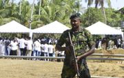 Terwijl achter hem de begrafenis plaats vindt van een slachtoffer van de bomaanslagen, houdt in de stad Negombo een Srilankaanse militair de wacht.  beeld AFP, Lakruwan Wanniarachchi​