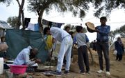 Vluchtelingen hebben een tent opgeslagen buiten het officiële kamp Moria, dat overvol is. Sommigen bakken zelf brood. beeld EPA, Stratis Balaskas