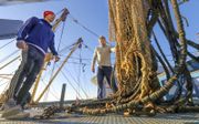 In Harlingen wordt de UK 227 omgebouwd van elektrisch vissen naar de verouderde boomkortechniek. Foto: schipper Simon van Slooten (r.) en bemanningslid Evert de Boer helpen bij het takelen van de pulsmodules.  beeld Simon Bleeker