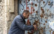 Nakash, een teruggekeerde christen, opent de zwaar gehavende kerkdeuren. Deze zijn doorzeefd met kogels en beklad. Islamitische Staat gebruikte de kerk als rechtbank en uitvalsbasis. beeld HVC, Jan Dirk van Nifterik