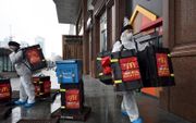 Werknemers van McDonalds bezorgden woensdag in beschermende kleding voedsel aan de inwoners van Wuhan, China. beeld AFP