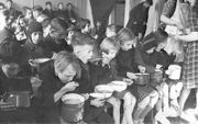 Kinderen eten een halve liter bijvoeding per dag tijdens de Hongerwinter, verschaft door het Interkerkelijk Bureau. Menno Huizinga was onderdeel van de Ondergedoken Camera en maakte illegaal foto’s tijdens de bezetting. Dit deed hij hoofdzakelijk in zijn 