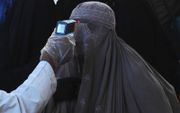 Een gezondheidsfunctionaris controleert de lichaamstemperatuur van een in een boerka geklede vrouw. beeld AFP, Arif Ali