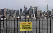Zicht op de skyline van Manhattan, New York, met op de voorgrond een bordje met de oproep afstand tot elkaar te houden. beeld AFP, Angela Weiss