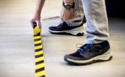 Een werknemer brengt tape op de werkvloer aan om te zorgen dat consumenten 1,5 meter afstand van elkaar houden. De 1,5 metereconomie zal het beeld in winkelstraten blijvend doen veranderen.  beeld ANP, Sem van der Wal