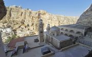 Het klooster van Mor Tekla ligt in de schaduw van een overhellende berg. Vanuit de grot waar het klooster omheen is gebouwd, is op de bergrug aan de overkant van de vallei het verwoeste hotel Safir te zien. Dat was het zenuwcentrum van Jabhat al-Nusra tij
