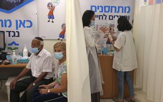 In Israël kunnen zestigers al om een derde dosis van het Pfizervaccin. Op de foto: een Israëlisch stel wacht op de derde prik bij de Clalit Health Service in Jeruzalem op 1 augustus 2021.  beeld AFP, Menahem Kahana