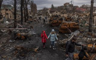 Oekraïense burgers lopen tussen de puinhopen in Boetsja, een voorstad van Kiev. Russische soldaten hebben daar tientallen burgers geëxecuteerd.  beeld EPA, Roman Pilipey