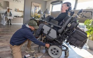 Een zorgverlener sluit de rolstoel van Dick Cochius aan. beeld APA Foto, Sjef Prins