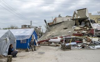 De gevolgen van de aardbeving in Turkije zijn nog volop tastbaar. Abuzer Dede (tweede van links), zit voor zijn tent na zware regenval in Adiyaman in Zuidoost-Turkije. Enkele weken geleden trof een aardbeving met een magnitude van 7,8 de regio. Honderdduizenden Turkse overlevenden zijn ondergebracht in tenten en containerwoningen. beeld AFP, Bulent Kiliç