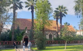 De protestantse kerk in Izmir, Turkije, met haar oranje dakpannen, omheind door bomen, waar een aantal mensen voorbijlopen.