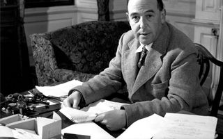 Zwartwitfoto van een kalende man in pak achter een bureau met allerlei paperassen.