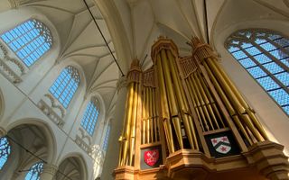 In een kerk met hoge, witte gewelven is een imposant pijporgel met koperkleurige pijpen de blikvanger.