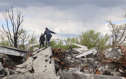 Oekraïense tieners lopen op de brokstukken van een gebombardeerd gebouw in een dorp in de buurt van Charkov. beeld EPA, Sergey Kozlov
