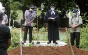 Een Indonesische predikant spreekt op het graf van een overleden coronapatiënt. Bijna alle landen op de wereld hadden de afgelopen anderhalf jaar te maken met hogere sterfte tijdens de pandemie.  beeld EPA, Hotli Simanjuntak