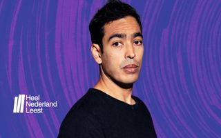 Foto van een getinte jonge man met zwart haar en een zwart shirt tegen een paarse achtergrond.