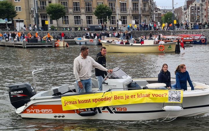 Motorbootje met vier inzittenden vaart op het water met een spandoek met de tekst: Jezus komt spoedig! Ben je er klaar voor? 