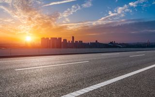 Lege asfaltweg met op de achtergrond hoge gebouwen en een ondergaande zon.