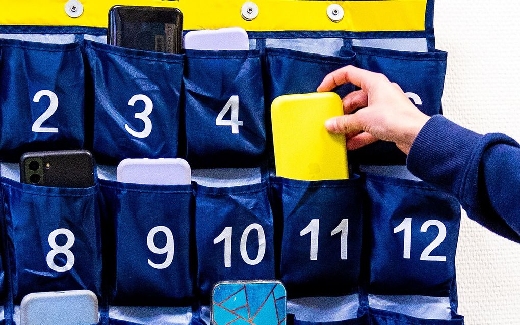 Een leerling bergt zijn mobieltje op in een telefoonzak. Het landelijk verbod op het gebruik van mobiele telefoons in de klas krijgt veel steun van ouders. beeld ANP, Iris van den Broek