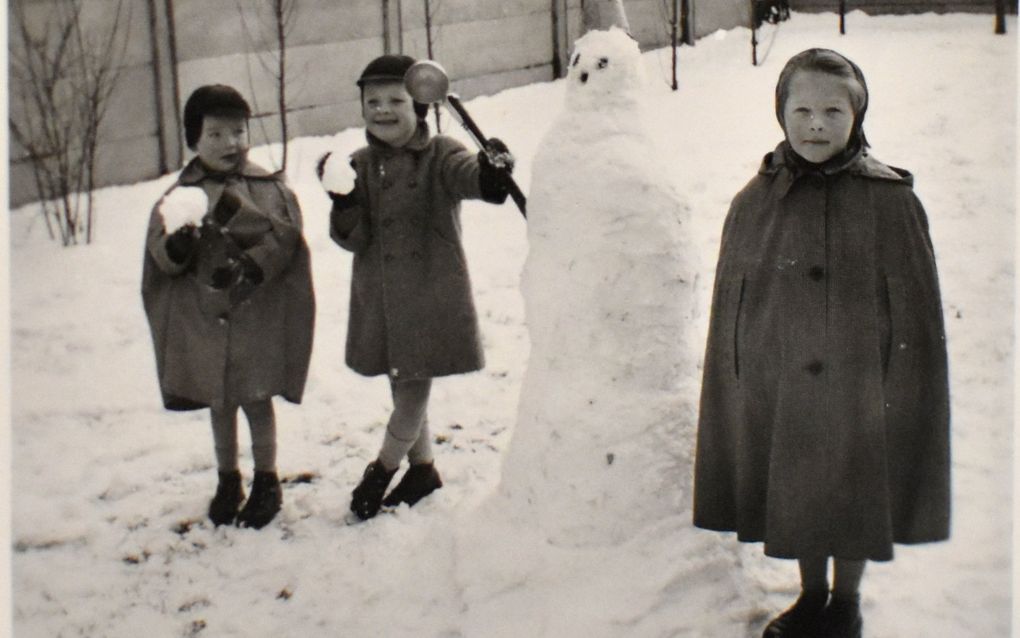Drie kinderen in warme winterjassen staan bij een sneeuwpop die net zo groot is als zijzelf.
