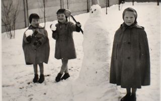 Drie kinderen in warme winterjassen staan bij een sneeuwpop die net zo groot is als zijzelf.