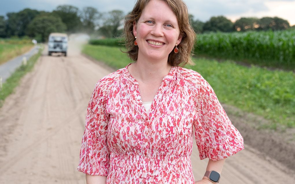 Vrouw in roze-rode jurk op een zandweg langs een maisveld