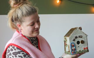 Vrouw in fleurige kleding houdt aardewerken vogelhuisje vast.