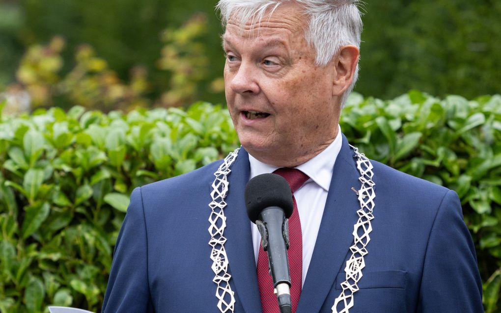 Man met ambtsketen spreekt voor microfoon.