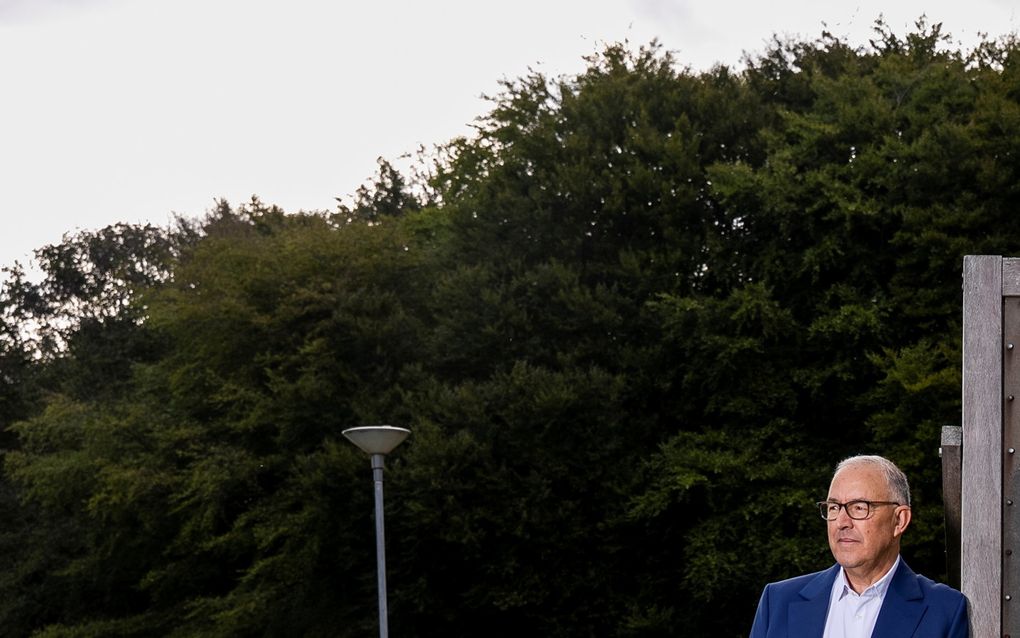 Man leunt tegen een houten paal aan. Hij kijkt naar links.